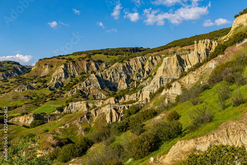 Fotografie Scenic view of eroded volcanic tuff formations and green hills under blue sky