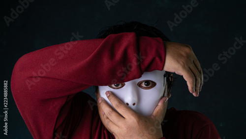 Obraz na plátně A secretive man wearing a blank white mask shields his eyes with one arm under moody lighting against a dark green textured backdrop, portraying an extreme defensive barrier