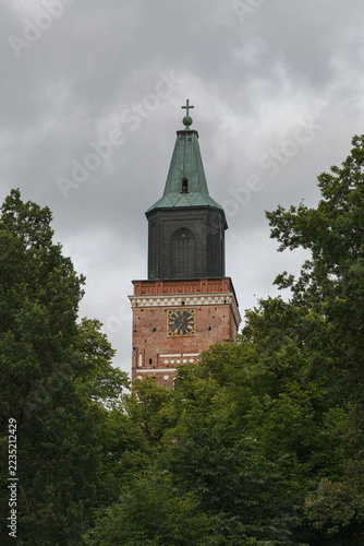 Turku Cathedral brick tower stands framed by green summer foliage.