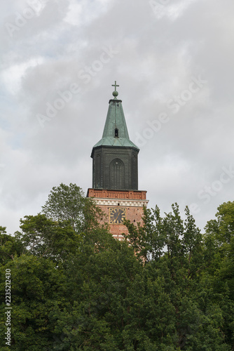 Turku Cathedral tower rises above tall trees under an overcast summer sky.