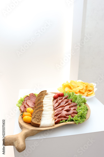 Meat platter with sliced sausage, ham and bread, accompanied by cherry tomatoes, lettuce leaves and potato chips.