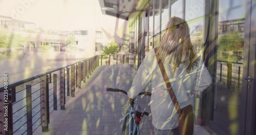 Woman in striped shirt wearing face mask holding blue bicycle beside metal railing on paved walkway