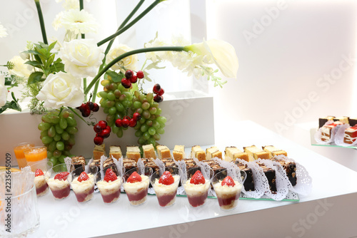 Assorted cream and strawberry desserts, chocolate pastries and sponge cake slices displayed on a festive table with grapes.