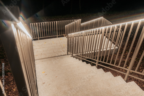 Obraz na plátně Illuminated concrete staircase descending between metal railings at night, with