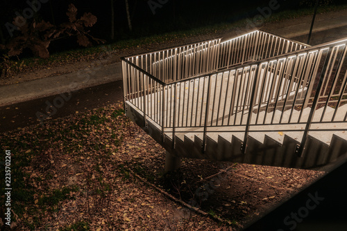 Obraz na plátně Illuminated outdoor stairway with metal railings descending beside a paved path,