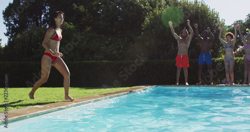 Diverse group of friends having fun jumping into a swimming pool
