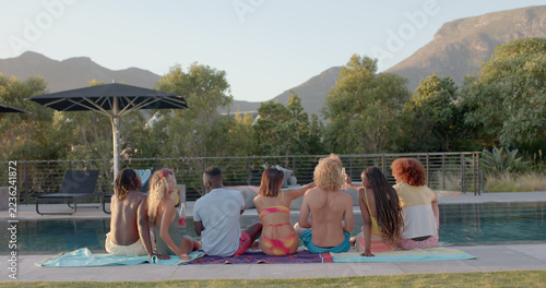 Happy diverse group of friends sitting and holding drinks by swimming pool