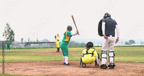 Diverse softball players and umpire waiting on community field holding bat, glove, mask