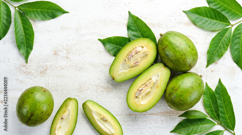 Fresh green feijoa fruits with sliced interiors and leafy branches arranged on a pale rustic surface for healthy food botanical tropical organic culinary harvest and natural lifestyle concepts