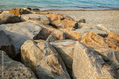 Obraz na plátně Large natural granite boulders forming a defensive barrier against waves on a pebble beach by the sea