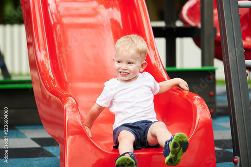 Fotografie Child sliding down playground slide, holding sides and looking forward, summer o