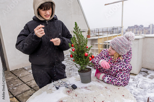Children decorate a small Christmas tree on a snowy rooftop