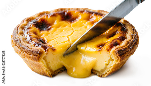 Close-up macro view of a Portuguese egg tart being sliced with a knife, showing warm oozing custard filling, isolated on a white background.