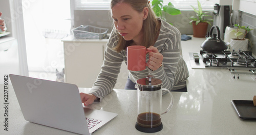 Caucasian lesbian couple holding coffee cups using laptop at home