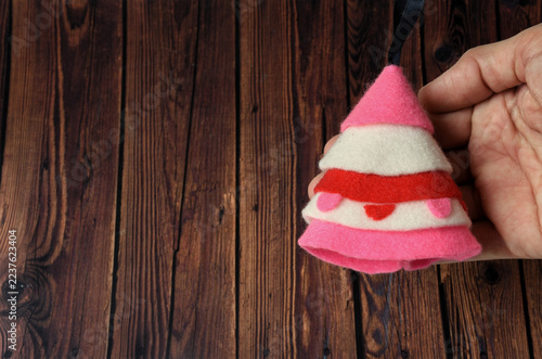 Cute pink and white felt tree with red trim, held by hand on a wood base.